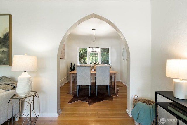 dining space with arched walkways, baseboards, and wood finished floors