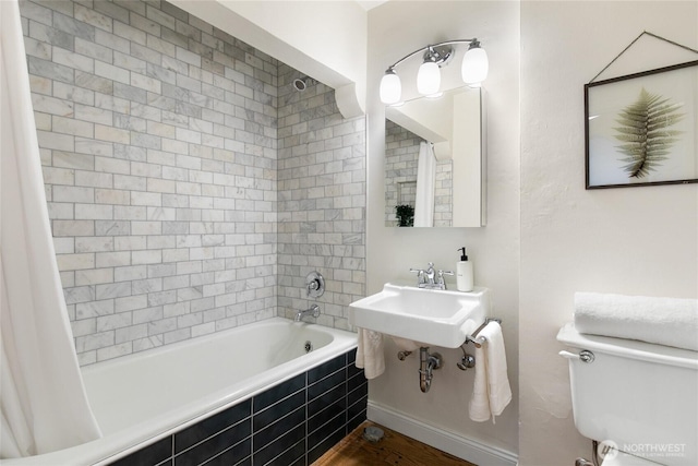 bathroom featuring toilet, tiled shower / bath, a sink, and wood finished floors