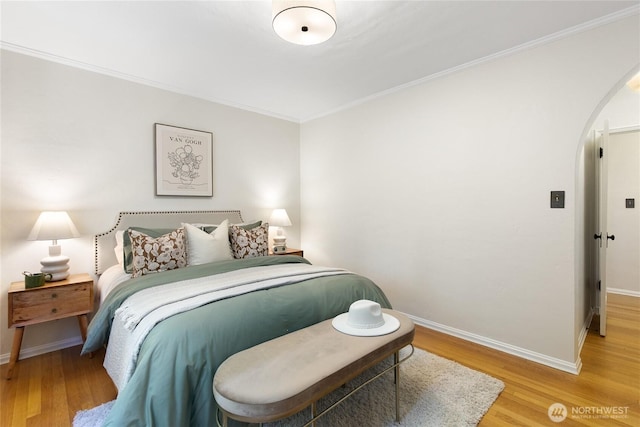 bedroom with arched walkways, baseboards, ornamental molding, and light wood finished floors