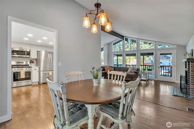 791 NE Pinecrest Dr, Bremerton, WA 98311 - dining area featuring vaulted ceiling, light wood finished floors, a chandelier, a fireplace, and baseboards