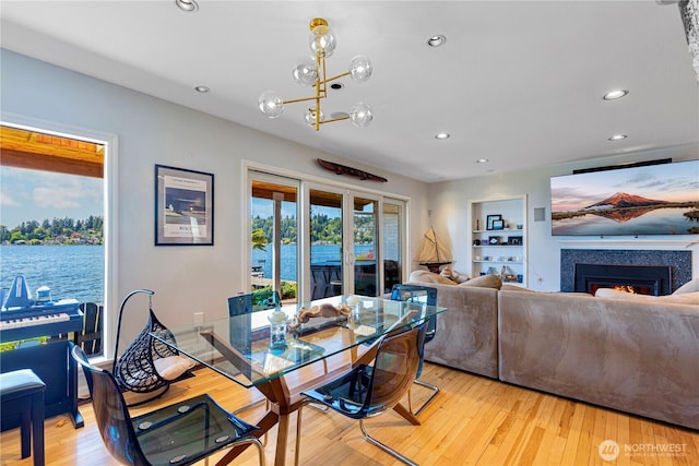 dining room with recessed lighting, a warm lit fireplace, a notable chandelier, and light wood-style flooring