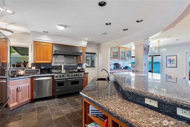 kitchen featuring brown cabinets, a sink, wall chimney exhaust hood, stainless steel appliances, and backsplash