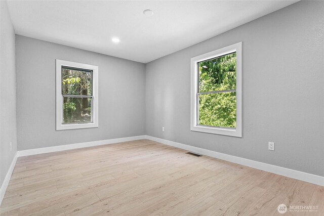 spare room featuring a healthy amount of sunlight, baseboards, light wood-style floors, and visible vents