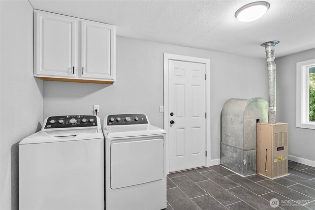 clothes washing area featuring a textured ceiling, baseboards, washing machine and dryer, and cabinet space