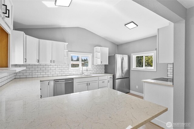 kitchen with decorative backsplash, lofted ceiling, light stone countertops, a sink, and stainless steel appliances