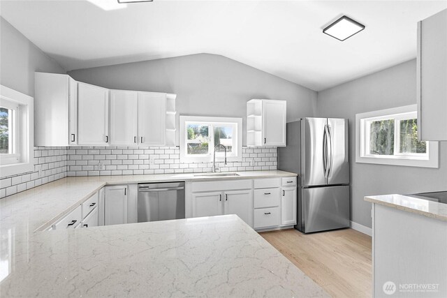 kitchen with open shelves, light stone countertops, a sink, light wood-style floors, and stainless steel appliances