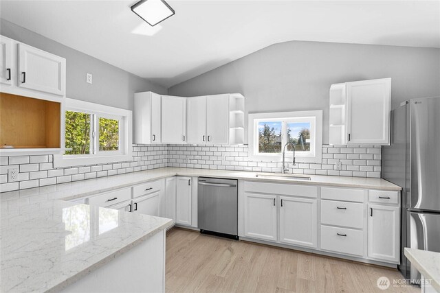 kitchen with open shelves, lofted ceiling, light stone counters, a sink, and appliances with stainless steel finishes