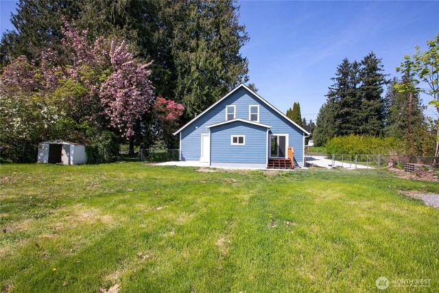 back of house featuring a storage unit, an outdoor structure, fence, and a yard