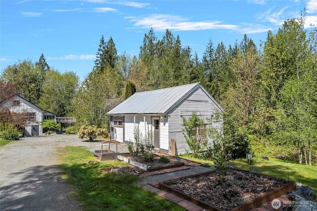 view of front of home featuring an outbuilding, a garden, metal roof, and a front lawn