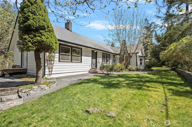 single story home featuring a shingled roof, a front lawn, and a chimney