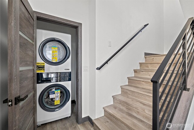clothes washing area featuring baseboards, laundry area, wood finished floors, and stacked washer and clothes dryer