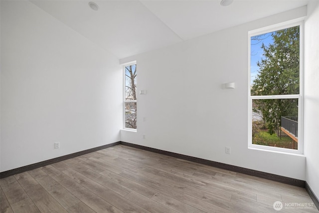 spare room with baseboards, vaulted ceiling, and wood finished floors