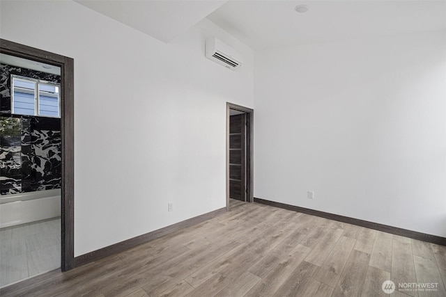 spare room with baseboards, a wall mounted AC, and wood finished floors