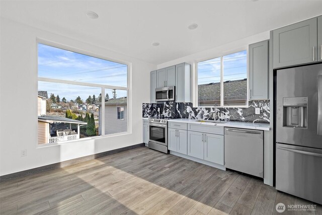 kitchen featuring decorative backsplash, appliances with stainless steel finishes, light countertops, a sink, and light wood finished floors