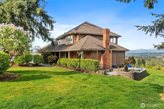 back of property featuring a lawn, roof with shingles, a mountain view, and a chimney