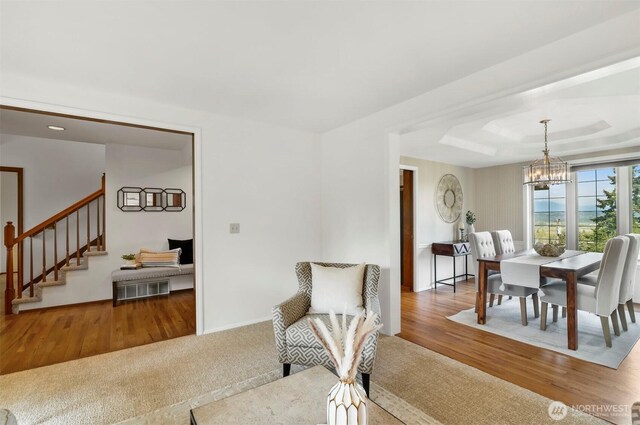sitting room with a raised ceiling, stairs, wood finished floors, and a notable chandelier