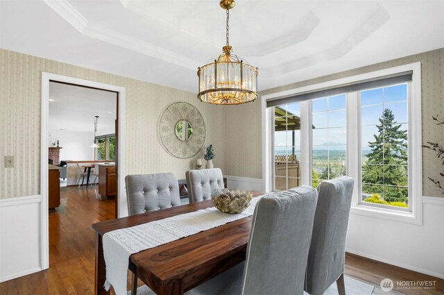 dining space with a raised ceiling, wallpapered walls, wood finished floors, and a notable chandelier