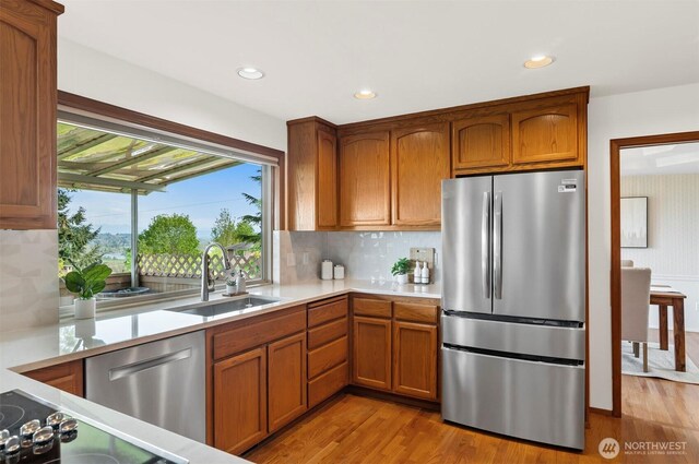 kitchen with appliances with stainless steel finishes, a sink, light countertops, brown cabinetry, and light wood-style flooring
