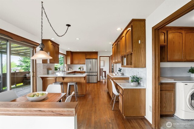 kitchen with freestanding refrigerator, washer / dryer, a peninsula, light countertops, and a sink