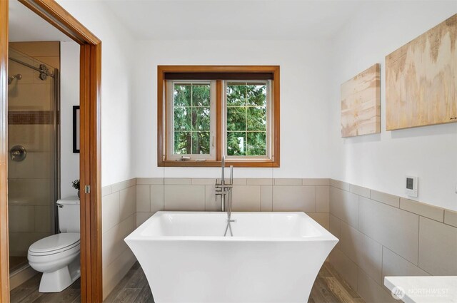 bathroom featuring a wainscoted wall, wood finished floors, tile walls, and a shower stall
