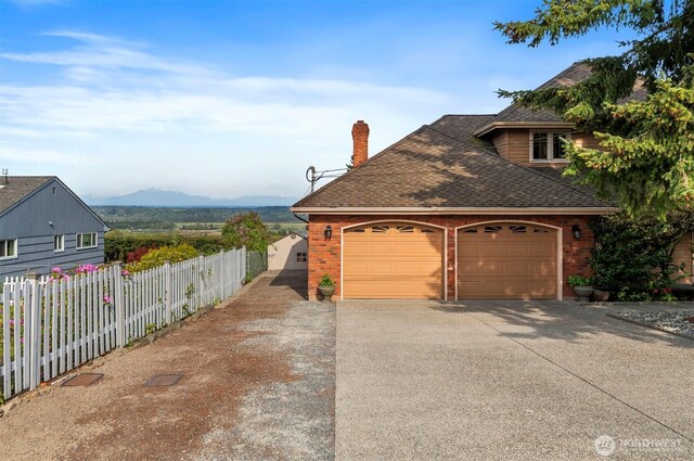 view of side of property featuring a chimney, brick siding, fence, a mountain view, and a shingled roof