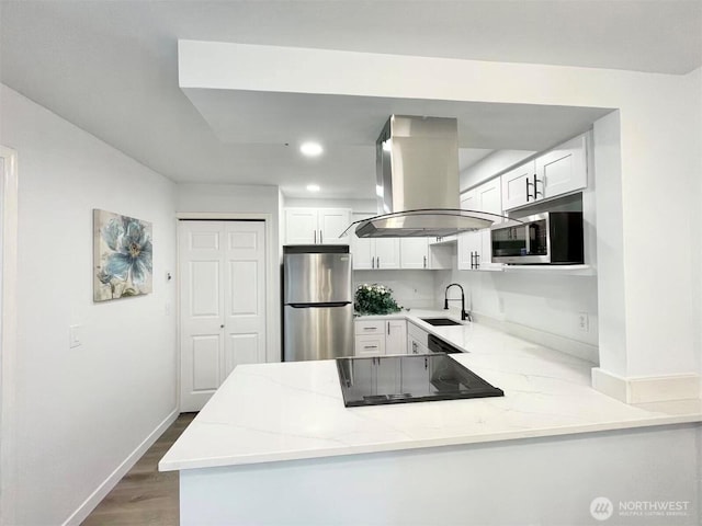 kitchen with stainless steel appliances, island range hood, a sink, light stone counters, and a peninsula