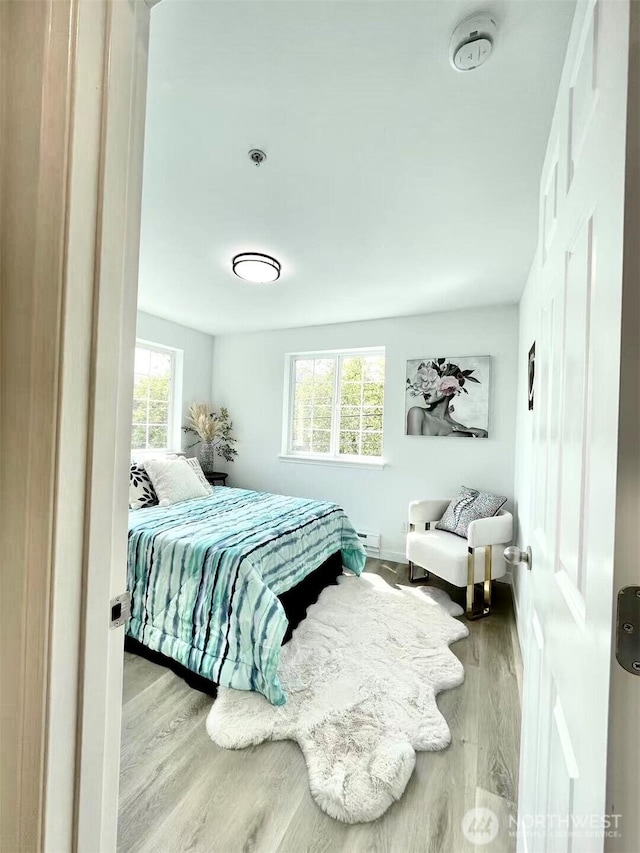 bedroom with wood finished floors, baseboards, and a baseboard heating unit