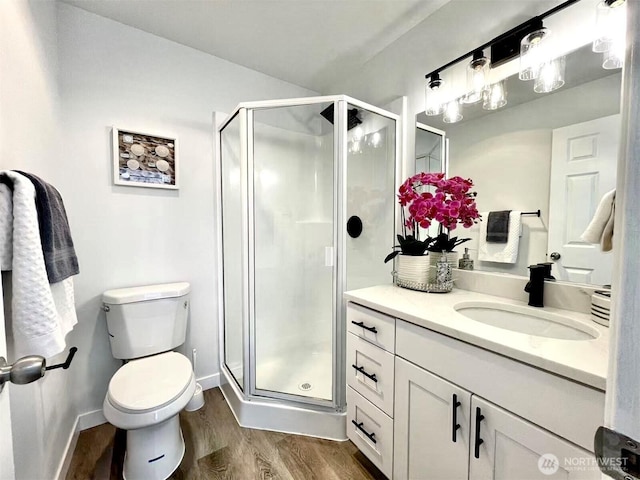 full bath featuring wood finished floors, a stall shower, vanity, toilet, and baseboards