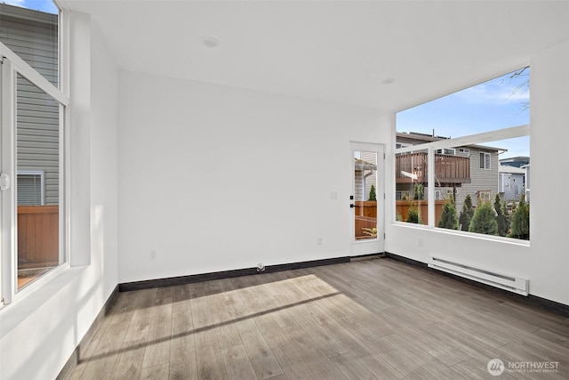 empty room with baseboards, baseboard heating, and wood finished floors