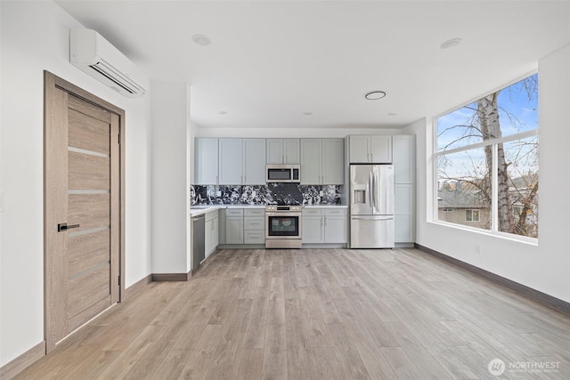 kitchen with light countertops, an AC wall unit, light wood-style flooring, stainless steel appliances, and gray cabinetry