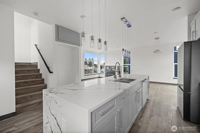 kitchen featuring light stone counters, a sink, appliances with stainless steel finishes, and wood finished floors
