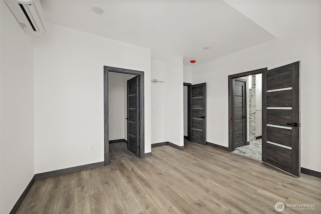unfurnished bedroom featuring light wood-style floors, baseboards, and a wall mounted air conditioner
