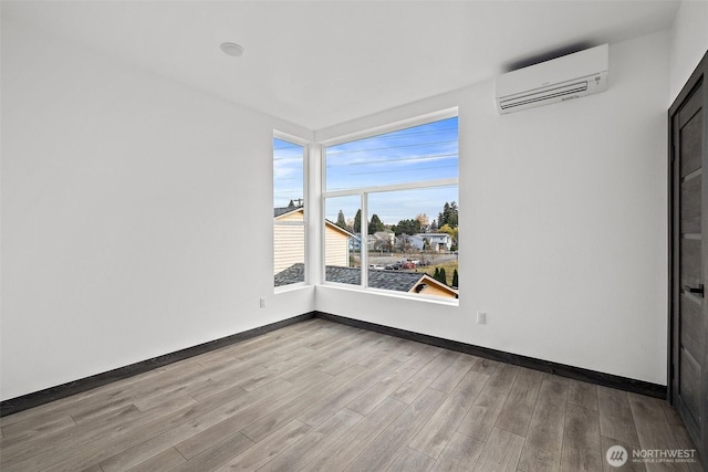 empty room with wood finished floors, baseboards, and a wall unit AC