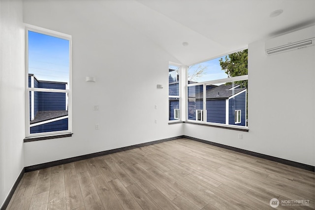 unfurnished room featuring baseboards, vaulted ceiling, a wall mounted air conditioner, and wood finished floors