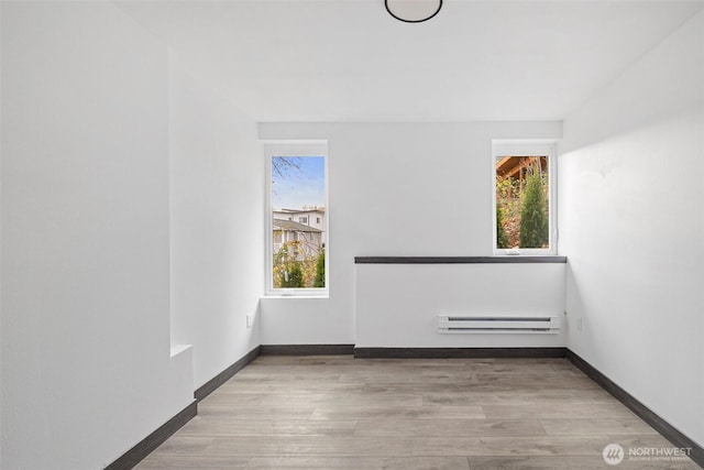 spare room with baseboards, a baseboard radiator, and wood finished floors