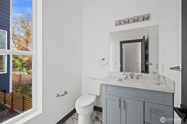 half bath featuring baseboards, vanity, toilet, and marble finish floor