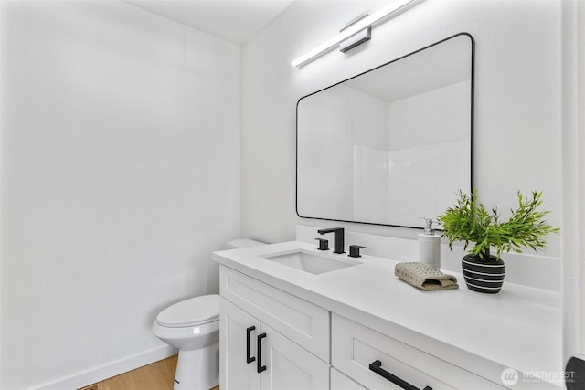 bathroom featuring vanity, baseboards, wood finished floors, and toilet