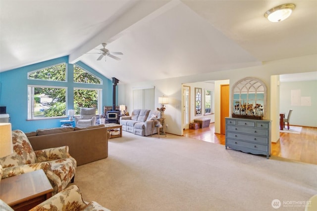 carpeted living room with vaulted ceiling with beams, a wood stove, and a ceiling fan