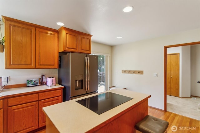 kitchen with brown cabinets, light wood finished floors, stainless steel fridge with ice dispenser, light countertops, and black electric cooktop