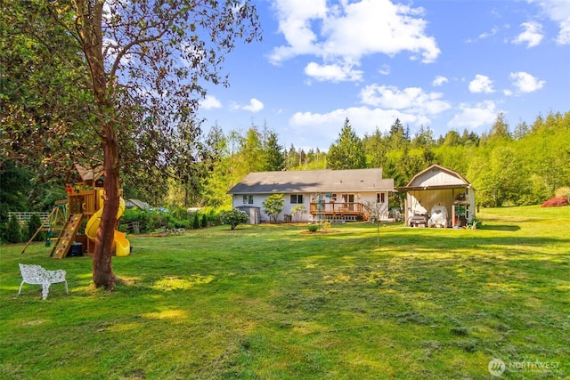 rear view of property with a playground, a yard, and a deck