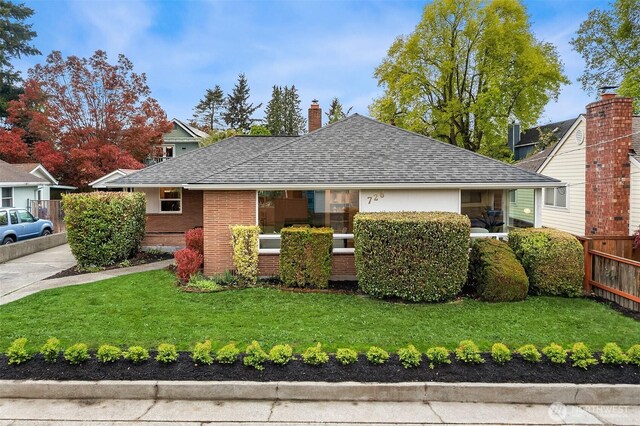 view of front of property with fence, a shingled roof, a front lawn, brick siding, and a chimney