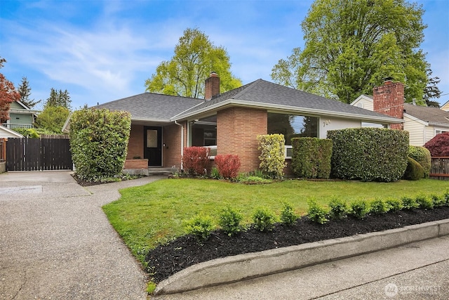 single story home featuring fence, a shingled roof, a front lawn, brick siding, and a chimney