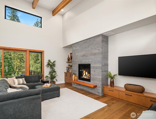 living area featuring a healthy amount of sunlight, a high ceiling, beamed ceiling, and wood finished floors