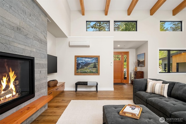 living room featuring plenty of natural light, a wall mounted AC, wood finished floors, beam ceiling, and a glass covered fireplace