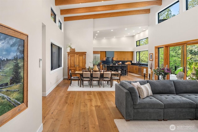 living area with light wood-style flooring, a high ceiling, and beam ceiling