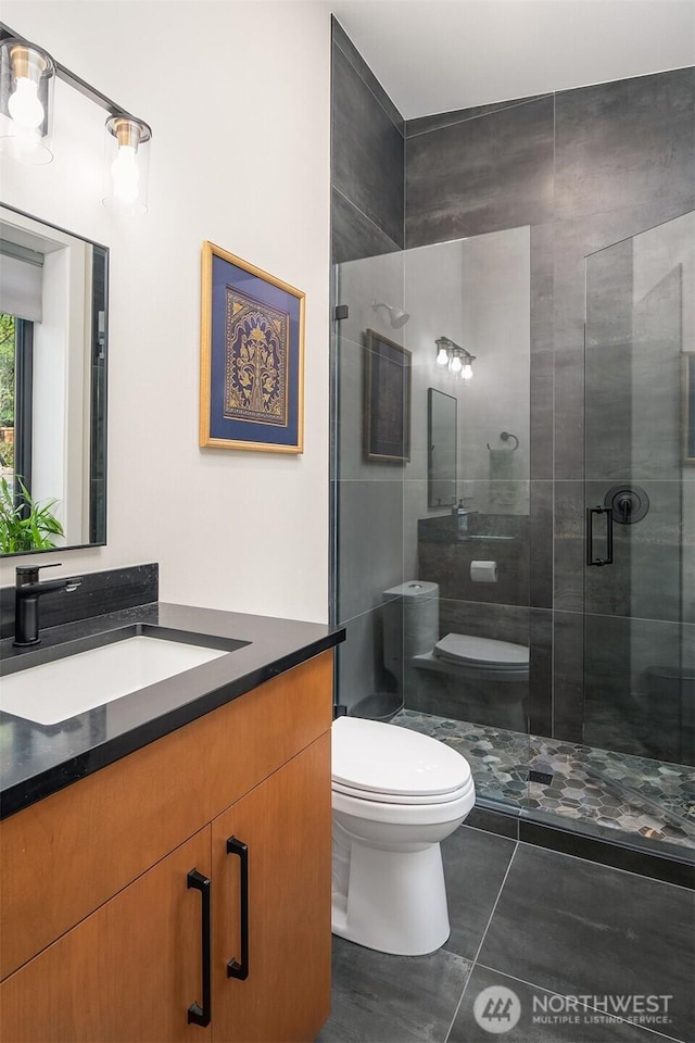 bathroom featuring vanity, toilet, tile patterned floors, and a stall shower