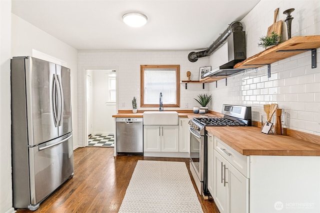 kitchen featuring open shelves, butcher block countertops, wall chimney range hood, a sink, and stainless steel appliances