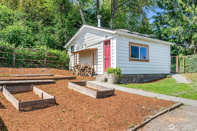 view of outdoor structure with fence, a garden, and an outbuilding