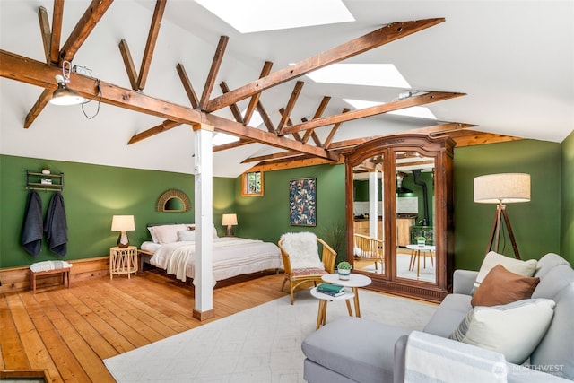 bedroom featuring wood-type flooring, access to exterior, and vaulted ceiling with skylight