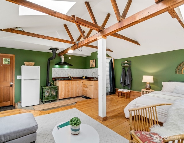 living room with a wood stove, vaulted ceiling with beams, and light wood finished floors